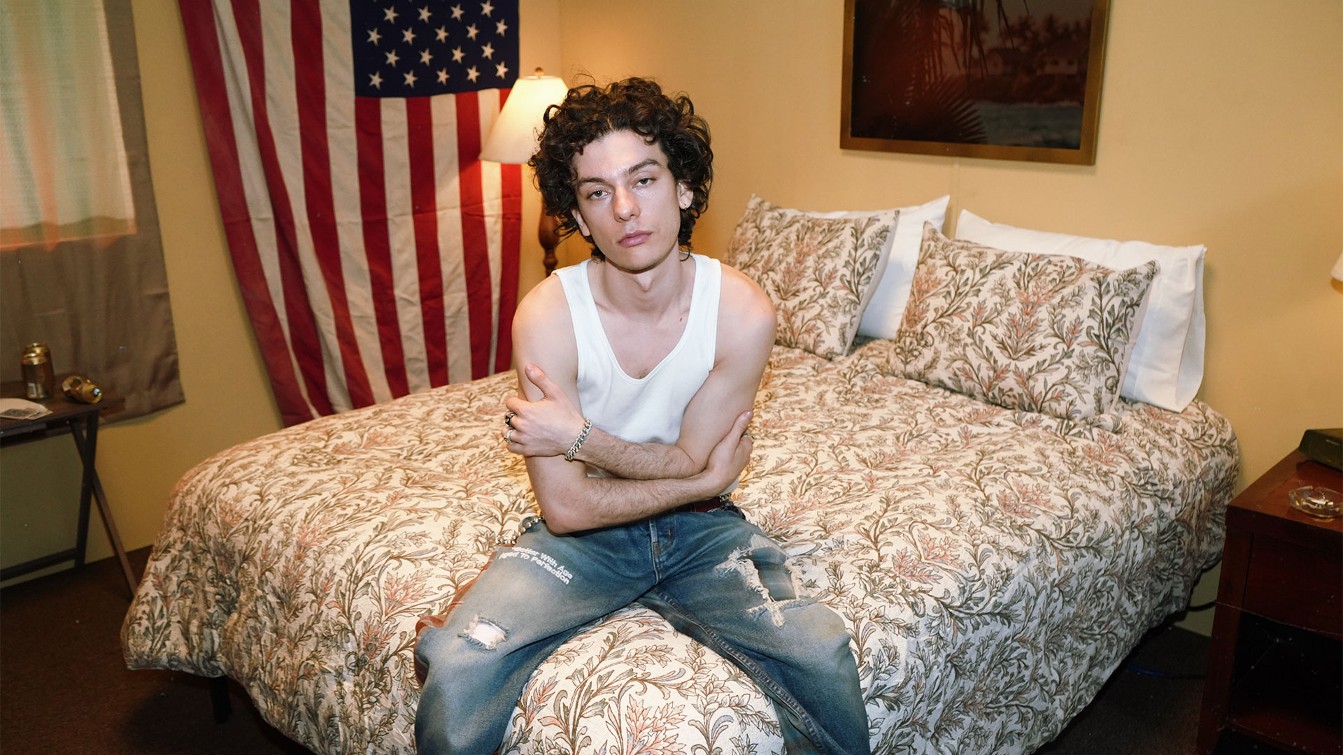 Henry Morris sitting on a motel bed under an American flag