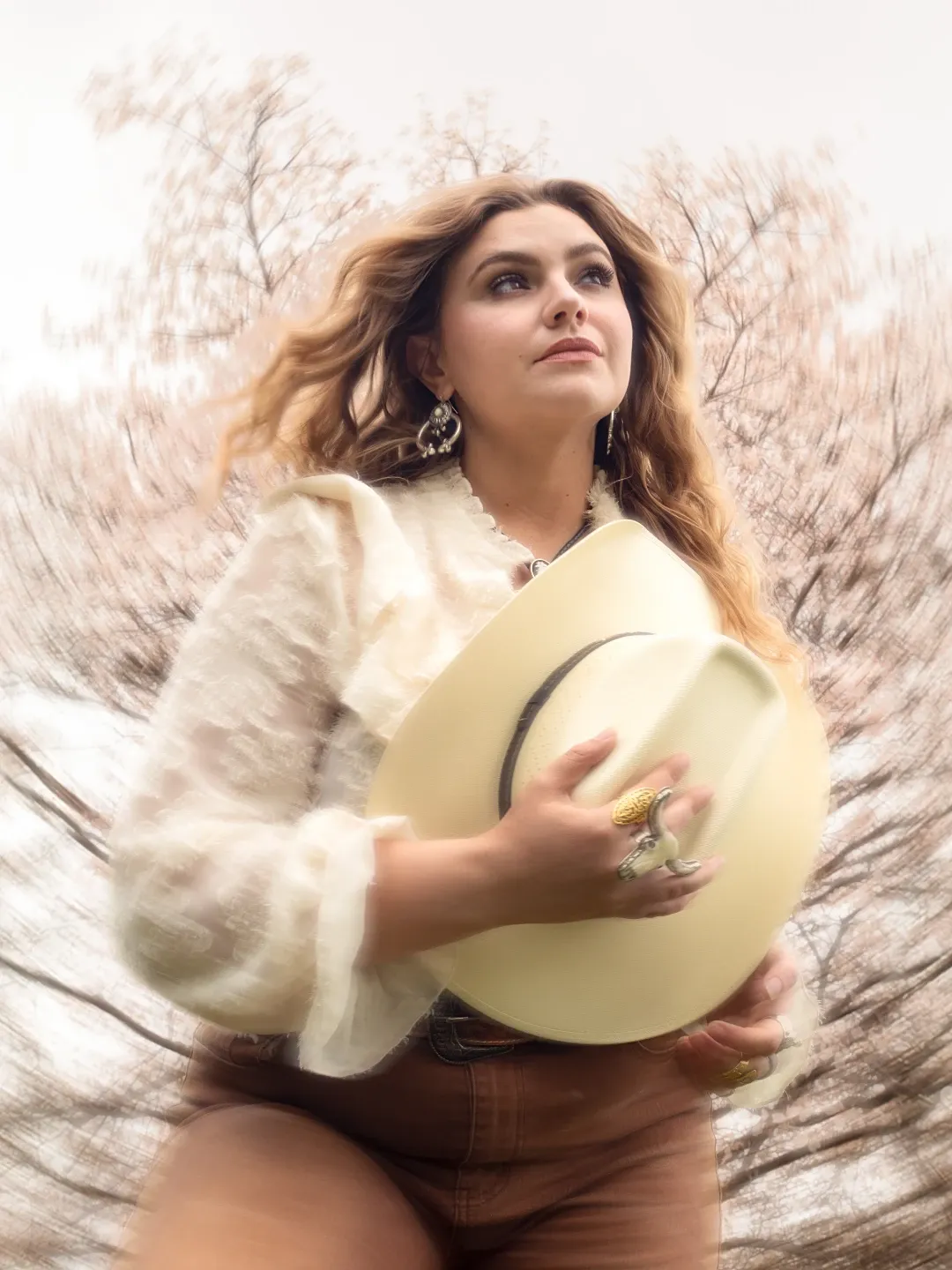 Nancy Ann holding a white cowboy hat under blossoming trees