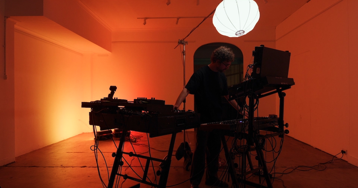 Voix Nulle playing a hardware synth setup in an orange-lit room