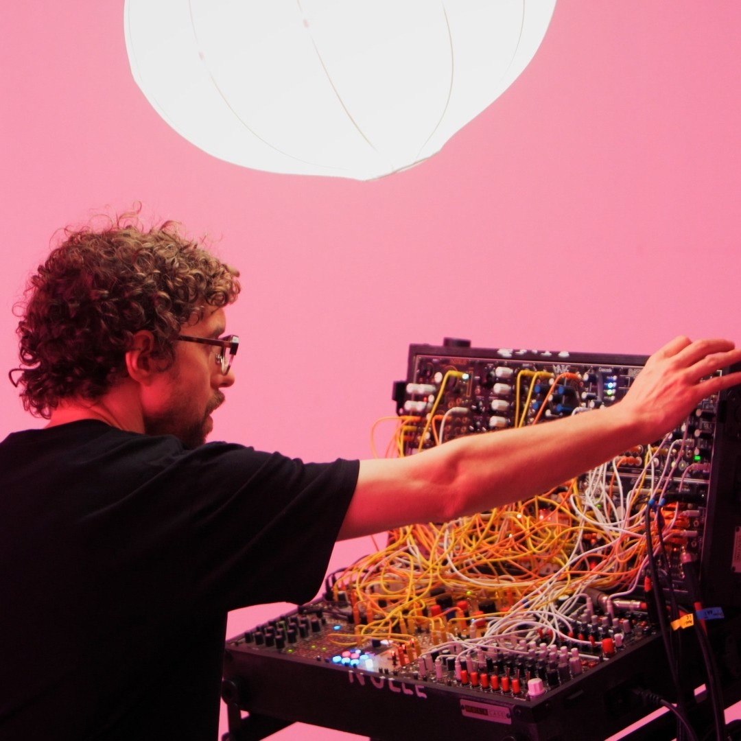 Voix Nulle patching a modular synthesiser against a pink wall